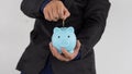 The hand put a coin into the glass piggy bank of a businessman in a black suit