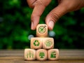 Hand put green Net Zero target symbol on wood block pyramid stack with renewable element icons.