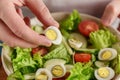 Hand put half of boiled quail egg into the bowl with fresh vegetables. Royalty Free Stock Photo