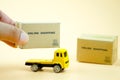 Hand put miniature cardboard boxes on yellow toy truck carries