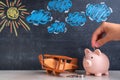 The hand puts a coin in the piggy bank. A wooden toy biplane airplane and a piggy bank stand side by side, a chalk board in the Royalty Free Stock Photo