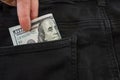 Hand puts 100 dollars in black jeans pocket. Close-up. Royalty Free Stock Photo