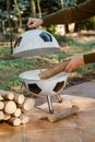 Hand puts piece of wood in round barbecue