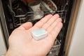 A hand puts a tablet in the dishwasher. Washing dishes in the kitchen. Royalty Free Stock Photo