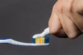 hand puts toothpaste on the toothbrush on a gray background close-up