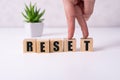 The hand puts a wooden cube with the letter R from the word Reset. The word is written on wooden cubes standing on the yellow