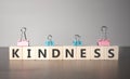 The hand puts a wooden cube with sign kindness. The word is written on wooden cubes standing on the dark table on the grey Royalty Free Stock Photo