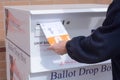 Hand putting ballot envelope into Jefferson County Colorado ballot drop box
