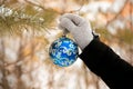 Hand putting blue decorated Christmas ball ornament on a Christmas tree