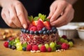 hand putting a cherry atop a mound of fruit tartare