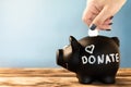 Hand putting a coin in a black piggy bank with a chalk donate tag on a blue background. Donation and charity concept Royalty Free Stock Photo