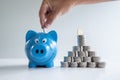 Hand putting coin in blue piggy bank with coins pyramid, step up growing business to success and saving for retirement concept Royalty Free Stock Photo