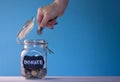 Hand putting a coin in a glass jar with coins with a chalk donate tag on a blue background. Donation and charity concept Royalty Free Stock Photo