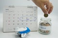 A hand putting a coin in a glass jar filled with coins labelled travel