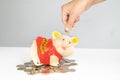 Hand putting coin into Orange piggy bank saving money with coins pile