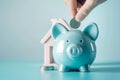 Hand putting a coin in piggy bank with house model. Saving money for buying a home, financial literacy. Budgeting, savings and Royalty Free Stock Photo