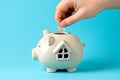 Hand putting a coin in piggy bank in a shape of a house. Saving money for buying a home, financial literacy. Budgeting, savings Royalty Free Stock Photo