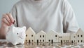 Hand putting coin into piggy bank and wooden house on wood table. Royalty Free Stock Photo