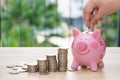 Hand putting a coin into a pink piggy bank with stack coins on w