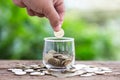 Hand putting coins into clear money jar on wooden table with green blur light background. Savings concept