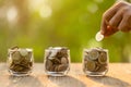 Hand putting coins into clear money jar on wooden table with green blur light background. Savings concept