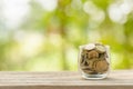 Hand putting coins into clear money jar on wooden table with green blur light background. Savings concept