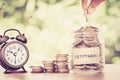 Hand putting Coins in glass jar with retro alarm clock for time Royalty Free Stock Photo