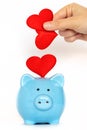 Hand putting many red heart into piggy-bank.