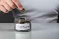 Hand putting penny in a coin jar. Coins in glass money jar with donations label. Glass jar full of money with white charity label Royalty Free Stock Photo