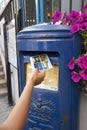 Hand putting a postcard in a Blue Guernsey Post Box unique to Guernsey in the town of St Pierre Port St Peter Port, the main Royalty Free Stock Photo