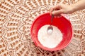 Hand putting sugar with spoon into red plastic bowl with wheat flour. Crochet tablecloth background. Top view. Copy space Royalty Free Stock Photo