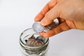 A hand putting some Indonesian coins in a glass of jar close up