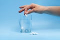 Hand putting white effervescent tablet or vitamin C into glass of water on blue background. Combating flu symptoms