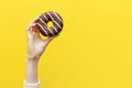 hand raises and holds one sweet donut in chocolate icing on yellow isolated background Royalty Free Stock Photo