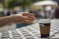 A hand reaches for dark vending coffee in disposable kraft paper cup and plastic lid on table at street cafe Royalty Free Stock Photo