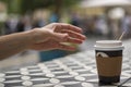 A hand reaches for dark vending coffee in disposable kraft paper cup and plastic lid on table at street cafe Royalty Free Stock Photo