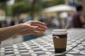 A hand reaches for dark vending coffee in disposable kraft paper cup and plastic lid on table at street cafe Royalty Free Stock Photo