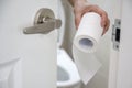 A hand reaches out for toilet paper in a beige tiled bathroom Royalty Free Stock Photo