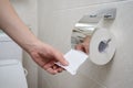 A hand reaches out for toilet paper in a beige tiled bathroom Royalty Free Stock Photo