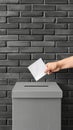 A hand reaches into a white ballot box and places a white ballot inside, in front of a stone wall Royalty Free Stock Photo