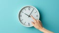 hand reaching out to a white wall clock on a light blue background, seemingly to adjust the time..AI generated image Royalty Free Stock Photo