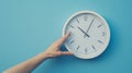 hand reaching out to a white wall clock on a light blue background, seemingly to adjust the time..AI generated image Royalty Free Stock Photo