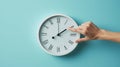 hand reaching out to a white wall clock on a light blue background, seemingly to adjust the time..AI generated image Royalty Free Stock Photo