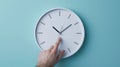 hand reaching out to a white wall clock on a light blue background, seemingly to adjust the time..AI generated image Royalty Free Stock Photo