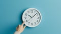 hand reaching out to a white wall clock on a light blue background, seemingly to adjust the time..AI generated image Royalty Free Stock Photo