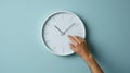 hand reaching out to a white wall clock on a light blue background, seemingly to adjust the time..AI generated image Royalty Free Stock Photo