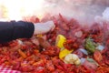 A hand reaching into a pile of steaming food piled on a table at a crawfish boil and grabbing a sausage