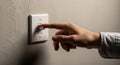 A hand reaching towards a light switch mounted on a textured beige wall. The switch Royalty Free Stock Photo