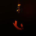 Hand reaching up to dim red light bulb Royalty Free Stock Photo