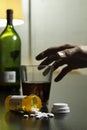 Hand reaching for wine and prescription pills on table, vertical